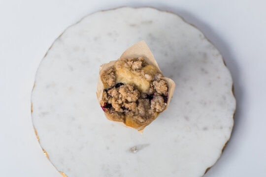One single delicious homemade baked blueberry muffin on a marble tray on white background