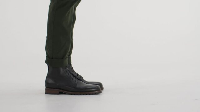 Man in black leather boots walking, stopping, and walking again, isolated on a white background in a studio side view