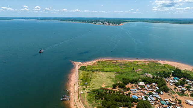 Aerial view of the shoreline and small settlement with boats docked along the sandy bank and the vast expanse of Lake Volta, Kwahu Afram Plains South, Eastern Region, Ghana.
