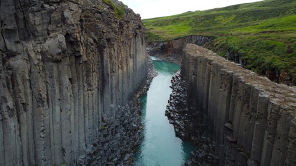 Obraz premium Close aerial view of hexagonal basalt column walls framing turquoise glacial river in Icelandic canyon