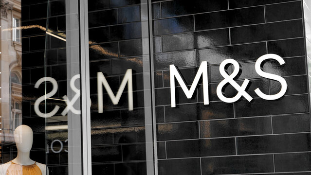 Manchester, England, UK - 18 June 2026: M&S Marks and Spencer storefront sign, white corporate logo letter text on black glossy brick tile wall facade shop exterior
