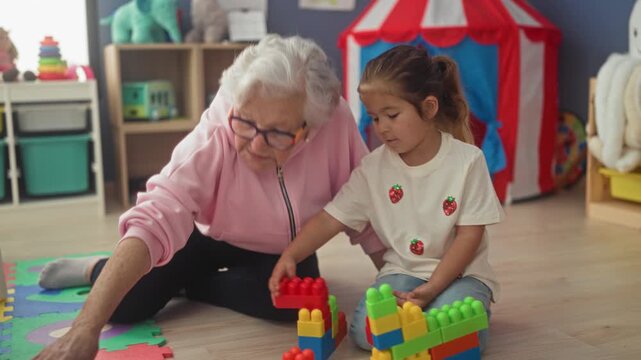 Woman building blocks with hand visible in playroom daycare setting, guiding child and stacking colorful toys; intergenerational bonding warmth.
