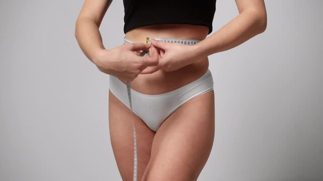 Woman measuring waist circumference for weight loss with measuring tape against a white background