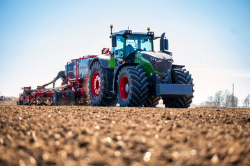 A green Fendt tractor with red wheels tows a red seed drill at dawn, LED beacons lit, oversized tires imprint soil, long shadows and cool light define planting season. © True Pixel Art