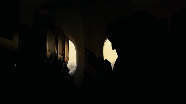 Passenger using phone on plane before takeoff, dramatic silhouette