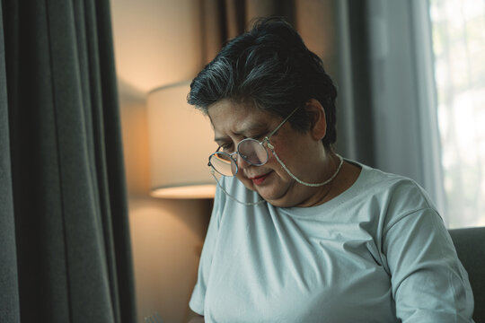Sad Elderly Asian Woman Sitting Alone with Bowed Head. Loneliness and Depression in Senior Life