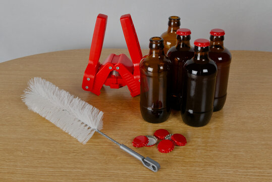 Grupo de botellas de cervezas artesanal, chapadora, limpiador de botellas y chapas rojas sobre mesa de madera