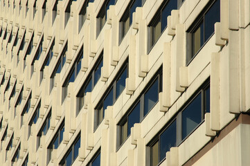 Fototapeta premium Close up diagonal view of a modern brutalist concrete skyscraper facade showing a geometric grid pattern of identical windows with dark glass.