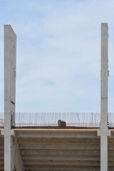 Naklejka premium Front view of two tall vertical precast concrete columns standing on a structural floor slab with exposed steel rebar grids against a bright sky.