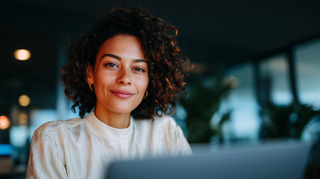 Confident professional Blasian woman working at a desk in a stylish modern office, warm approachable smile, engaged in a video conference call with a client on a laptop screen, ele
