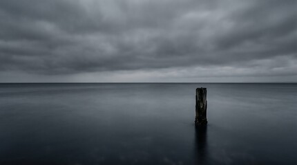Fototapeta premium Dark ocean water with single post under cloudy sky