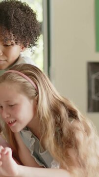 Vertical video: Leaning two students sharing handheld device in classroom, adjusting pink headband