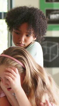 Vertical video: Reacting to peer shielding face in class, child behind leaning, soothing, pale top