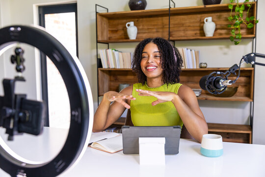 African American woman gesturing while recording in home studio with tablet, ring light and mic