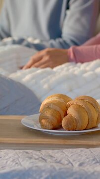 Vertical video: Starting with still tray, pink person moving hands across quilt at bed, croissants