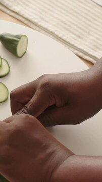 Vertical video: Starting holding blue knife, hands slicing cucumber on cutting board for white bowl