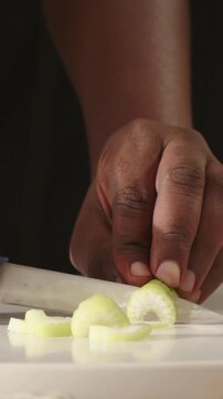 Vertical video: Slicing hand steadying pale green veg on board, cutting uniform slices with knife