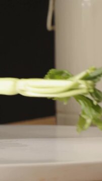 Vertical video: Slicing hands in dark top cutting celery on board at counter, chef's knife entering