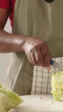 Vertical video: Placing cabbage on board, man in apron slicing with knife at home preparing meal