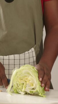 Vertical video: Holding halved cabbage, cook in apron shredding for salad at counter with knife