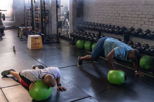 Two African American men in sportswear doing core drills at gym with green medicine balls