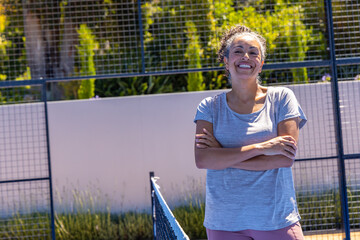 Middle-aged African American woman standing by net, smiling in sunny light on court, copy space