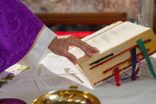 Priest in a purple vestment, a chasuble, turning pages in a Missal, a liturgical book of the Eucharistic prayer during Catholic Mass.