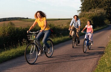 Fototapeta premium Mother, father, and two children cycling along a peaceful rural road through sunlit fields, cheerful family bicycle outing captured in warm evening light and open countryside