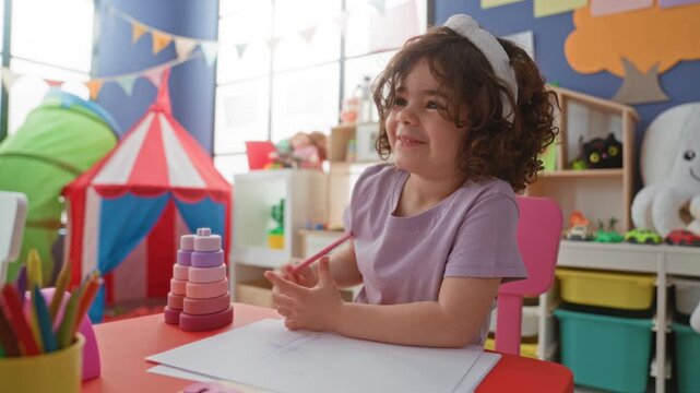 Girl drawing with pink crayon, hand tracing shapes on paper in a colorful playroom building; creative focus play.