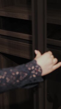 Vertical video. Female hand opening glass wardrobe door with modern storage furniture inside.