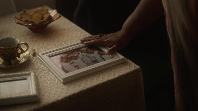 Closeup of African American senior woman gently touching framed family photograph on table. Clip is suitable for marketing campaigns focusing on senior mental health, nostalgia, and memory care
