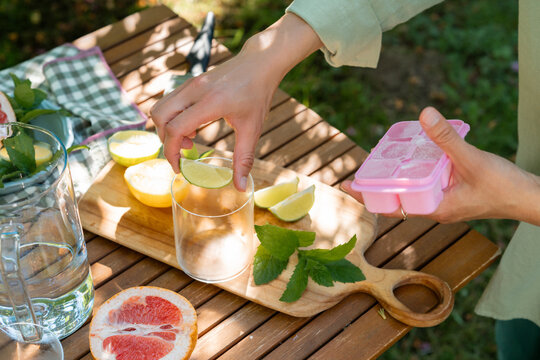 High angle cropped shot of a person holding a pink ice cube tray and putting a fresh lime slice into a glass
