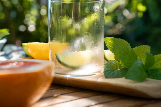 Close-up of a fresh lime slice in a glass with mint and sliced citrus fruits prepared on a wooden board outdoors