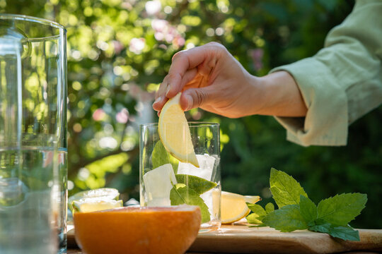 Person putting a fresh citrus slice into a glass with ice and mint to make a homemade summer cocktail