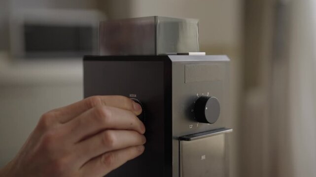 Close-up shot of hand turning adjustment dial on professional electric burr grinder, selecting ideal fineness for brewing coffee from fine to coarse settings. Shooting in slow motion