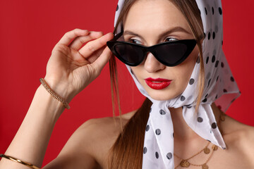 Naklejka premium Beautiful woman in stylish sunglasses and headscarf on red background