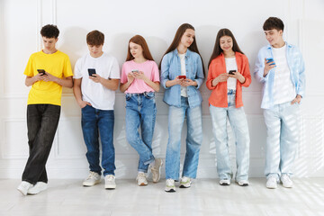 Obraz premium Group of teenagers with different smartphones near white wall indoors