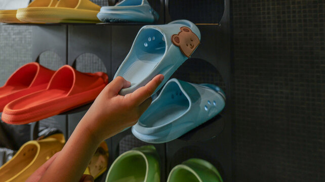 Child's hand selecting a cute blue slide with a bear face from a shoe rack