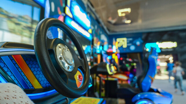 Close-up of a racing arcade game steering wheel with colorful lights in the background