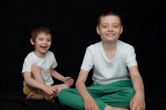 Two boys sit and smile happily against a dark background during a fun indoor moment