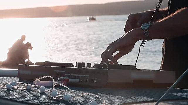 Close-up of DJ hands mixing on controller on at sunset, lake background with string lights. Summer party atmosphere.