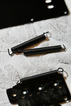 Close-up vertical photograph of disassembled electric guitar tremolo parts on a white cloth, showcasing black metal tension springs, a tremolo block bridge plate