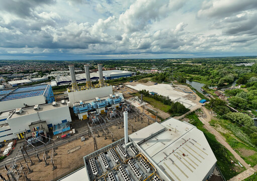 Aerial view of Rye House Power Station featuring tall chimneys, industrial infrastructure, and cooling units, set near a river and lush greenery, Hoddesdon, England, United Kingdom.