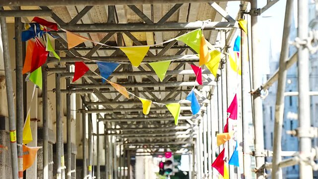 Festive party flags decoration wrapped around temporary building scaffolding tunnel structures symbolizing contrast between industrial work and festive event