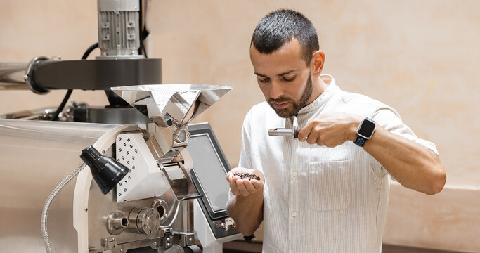 Caucasian man barista testing aroma of fresh coffee beans after roasting machine industry, small business cafe