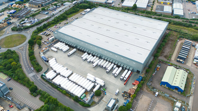 Aerial view of a large industrial warehouse facility with numerous white semi-trailers parked in the loading bays and surrounding yard in Hoddesdon, England, United Kingdom.