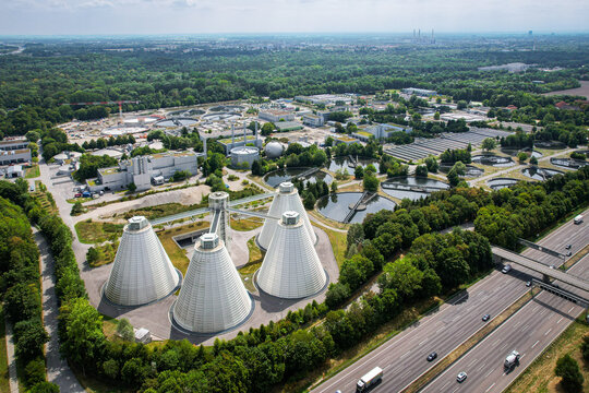 Aerial view of WWTP Gut Grosslappen wastewater treatment plant with conical digester tanks, surrounded by industrial infrastructure and forest near a highway in Munich, Bayern, Germany.
