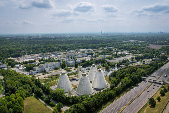 Aerial view of the WWTP Gut Grosslappen wastewater treatment plant with its distinctive conical digester tanks, surrounded by forests and adjacent to a highway in Munich, Bayern, Germany.