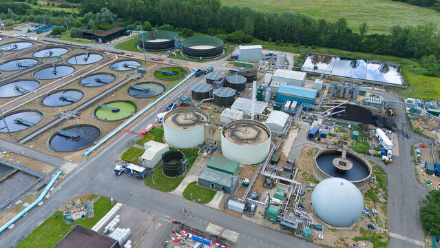 Aerial view of Alpheus Wastewater Sewage Treatment works featuring large circular sedimentation tanks, industrial buildings, and pipe infrastructure in Milton Keynes, England, United Kingdom.