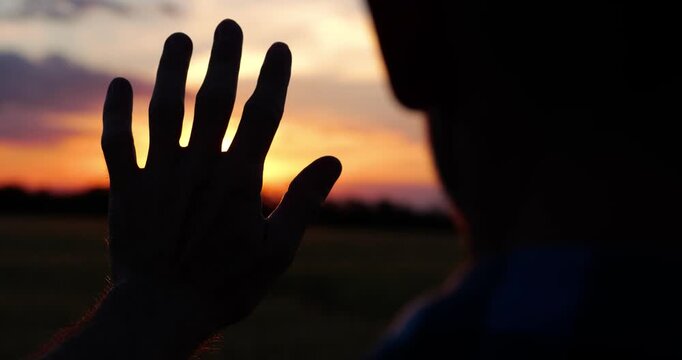 Man raises hand toward sunset horizon across open field. Powerful evening scene represents motivation, determination and commitment to achieving goals, overcoming challenges and moving forward.